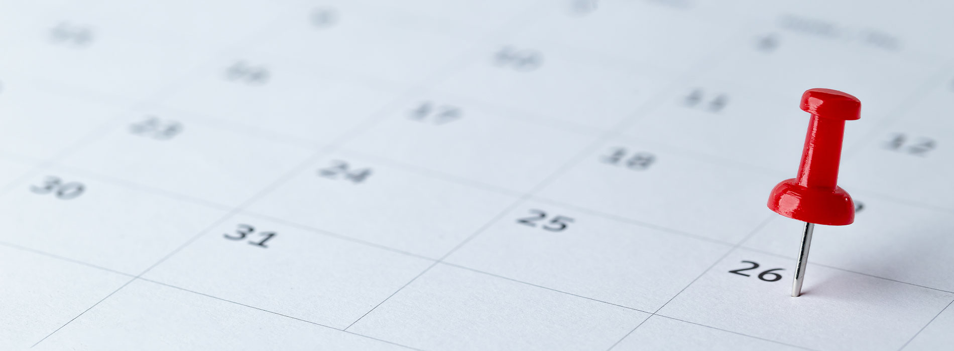 The image features a calendar with a red push pin marking a date on a white surface, indicating an event or reminder scheduled for that day.
