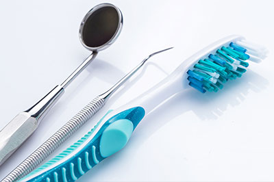 The image displays a collection of dental tools including a toothbrush, dental picks, and tweezers, along with a spoon-like instrument, all arranged on a white surface.