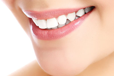 The image features a close-up of a person s face with a radiant smile, showcasing their teeth and lips, against a blurred background.
