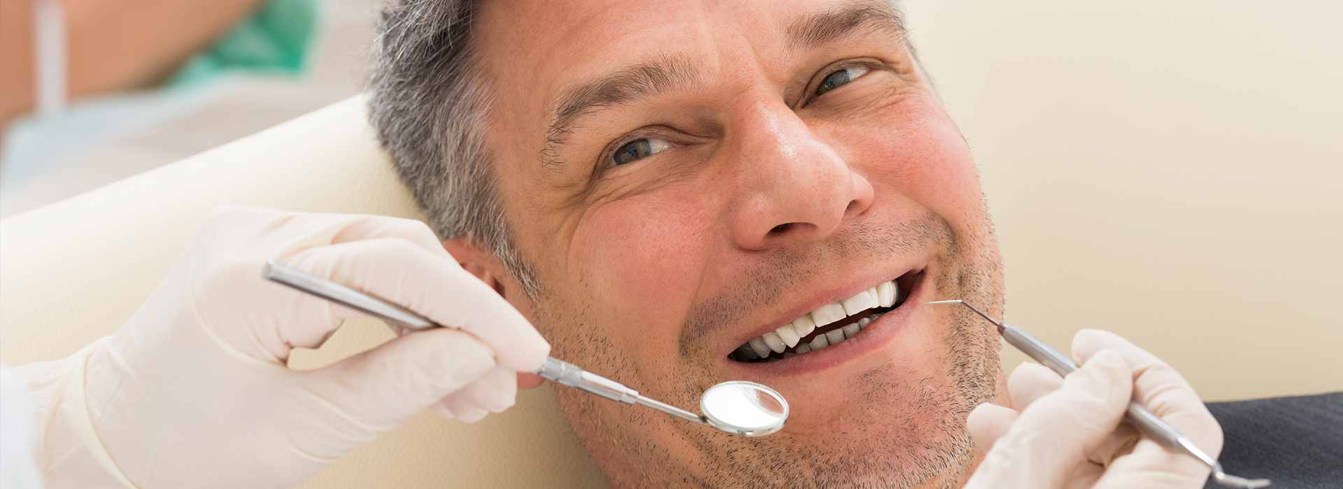 A man receiving dental care with a dentist using tools on his teeth while he smiles.