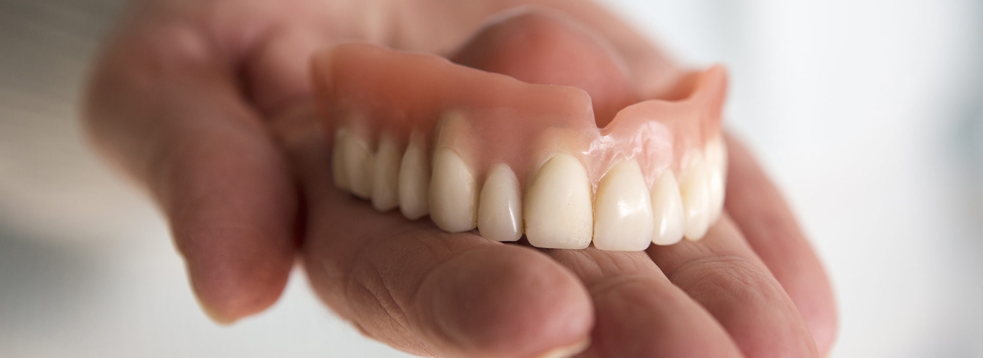 The image shows a person holding an open mouth displaying dentures, with a focus on the lower set of teeth.