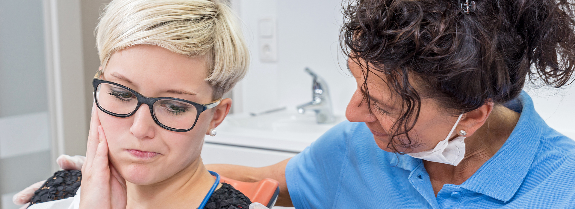 An elderly woman with glasses being examined by a dental hygienist in an office setting.