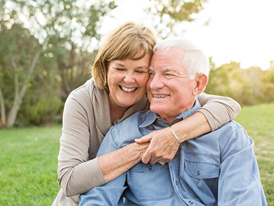 An elderly couple embracing warmly outdoors.