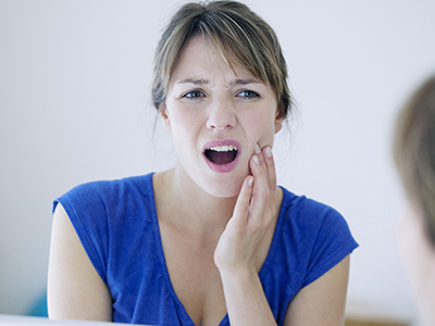 A woman with her mouth open, possibly screaming or expressing surprise, while looking at a reflection of herself in a mirror.