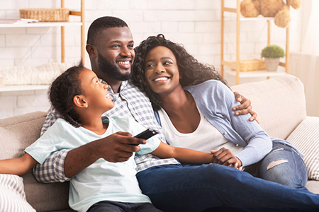 A family sitting together on a couch, with a man holding a child in his arms and a woman smiling at the camera.