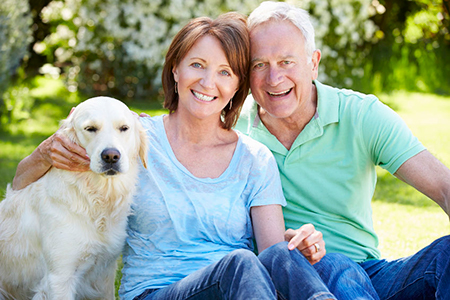 An older couple sitting outdoors with their golden retriever, smiling and posing for a photo.