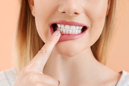 The image shows a woman with her finger on her teeth, possibly indicating dental care or oral hygiene.
