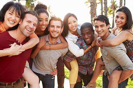 The image shows a group of people posing together for a photograph with smiles on their faces, outdoors during daylight.
