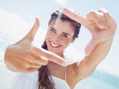 A woman with long hair, smiling, takes a selfie with her hand held up to the camera lens.